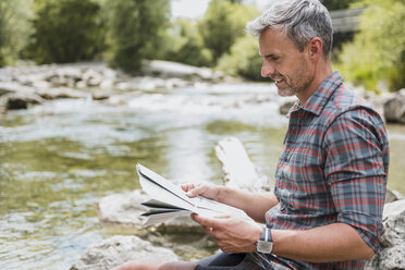 Hiker sitting at riverbank reading map - DIGF02607