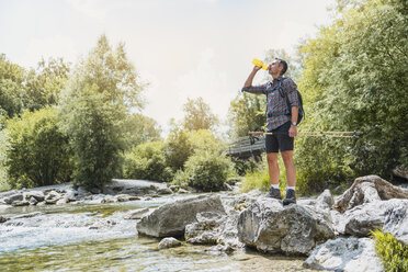 Hiker standing at the riverbank drinking from bottle - DIGF02611