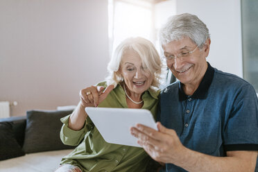 Happy senior couple at home sitting on couch sharing tablet - ZEDF00781
