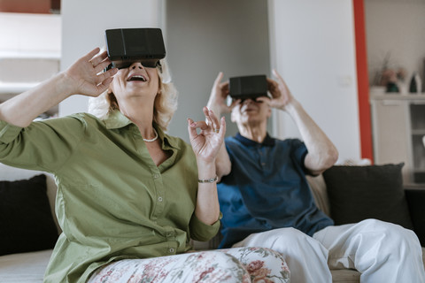 Happy senior couple at home sitting on couch wearing VR glasses stock photo