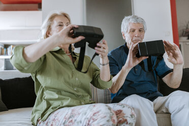 Senior couple at home sitting on couch holding VR glasses - ZEDF00784