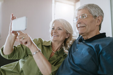 Senior couple at home sitting on couch taking a selfie - ZEDF00786