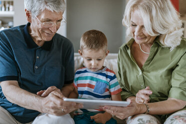 Grandparents and grandson at home sitting on couch sharing tablet - ZEDF00798