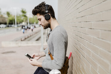 Junger Mann mit Rennrad und Kopfhörern, der ein Mobiltelefon benutzt - GIOF02971