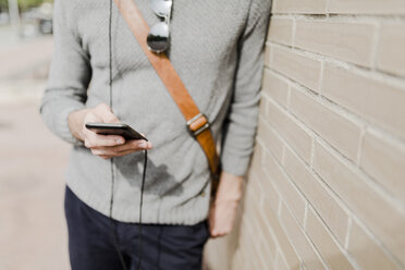 Young man with leaning against wall using cell phone, partial view - GIOF02973