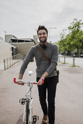 portrait of smiling young man with headphones pushing his bike - GIOF02974