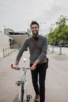 porträt eines lächelnden jungen Mannes mit Kopfhörern, der sein Fahrrad schiebt - GIOF02974