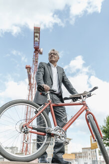 Porträt eines älteren Geschäftsmannes mit Fahrrad vor einem Baukran - GUSF00047