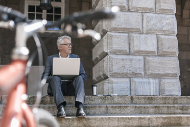 Älterer Geschäftsmann sitzt auf einer Treppe im Freien und arbeitet mit einem Laptop - GUSF00048