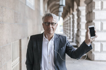 Portrait of senior businessman with earphones and smartphone - GUSF00055