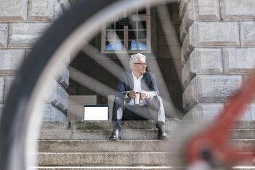 Älterer Geschäftsmann mit Fahrrad auf einer Treppe sitzend im Freien mit Laptop und Reisetasse - GUSF00057