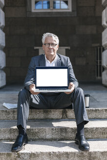 Porträt eines älteren Geschäftsmannes, der auf einer Treppe sitzt und einen Laptop zeigt - GUSF00059