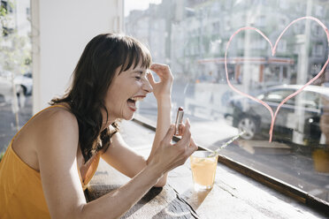 Frau sitzt im Café und malt mit Lippenstift ein Herz auf die Fensterscheibe - KNSF01882