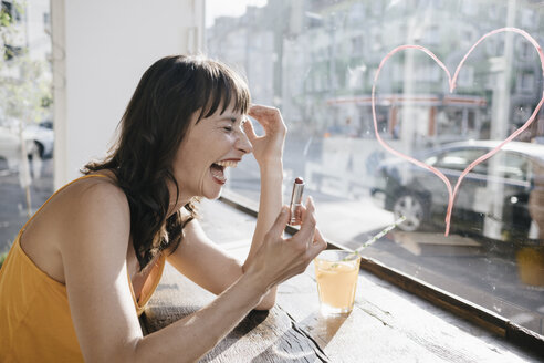 Woman sitting in cafe drawing heart shape on window pane with lipstick - KNSF01882