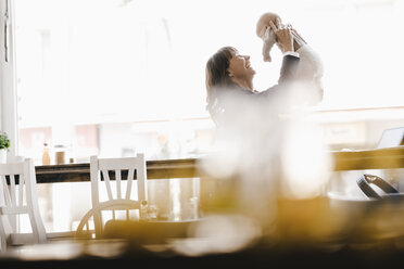 Businesswoman in cafe holding her baby aloft - KNSF01893