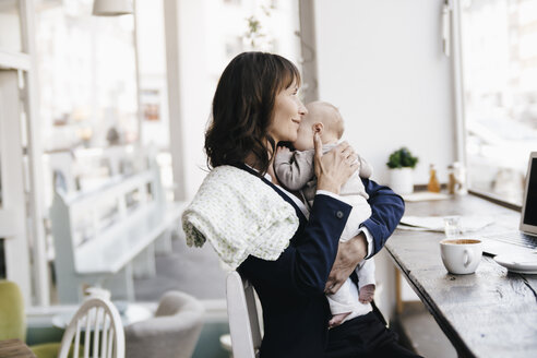 Geschäftsfrau im Café, die ihr Baby küsst - KNSF01894