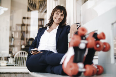 Businesswoman wearing roller skates, holding smartphone - KNSF01899