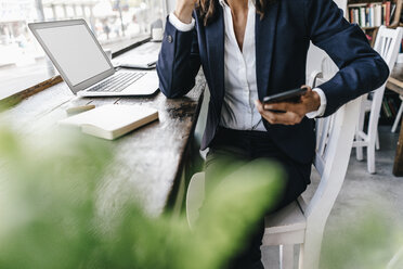 Businesswoman in cafe, using smartphone and laptop - KNSF01906