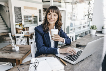 Businesswoman sitting in cafe using laptop and drinking coffee - KNSF01907