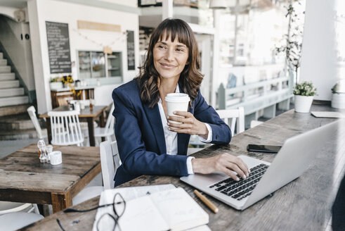 Geschäftsfrau, die in einem Café sitzt, einen Laptop benutzt und Kaffee trinkt - KNSF01907
