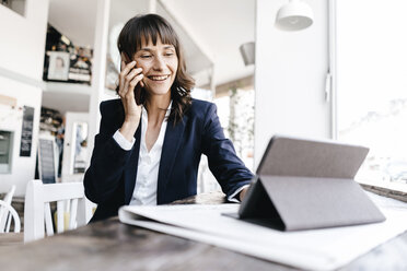 Businesswoman sitting in cafe with digital tablet, talking on the phone - KNSF01911