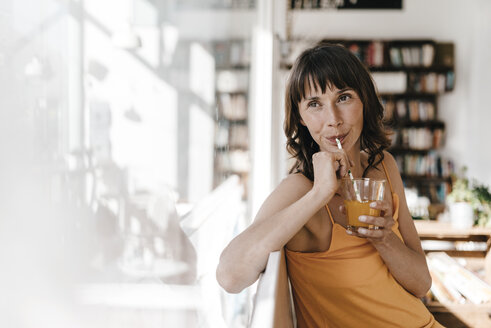 Frau sitzt in einem Café und trinkt aus einem Glas mit einem Strohhalm - KNSF01938
