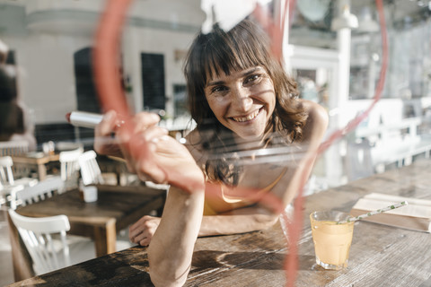 Frau sitzt im Café und malt mit Lippenstift ein Herz auf die Fensterscheibe, lizenzfreies Stockfoto