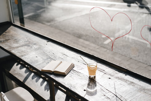 Book and drink on table in front of a window with lipstick hearts - KNSF01945