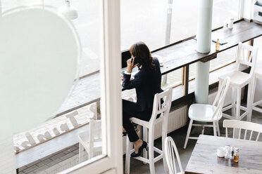 Businesswoman in cafe, using smartphone and laptop - KNSF01952