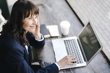 Geschäftsfrau sitzt in einem Café und benutzt einen Laptop, lächelnd - KNSF01954
