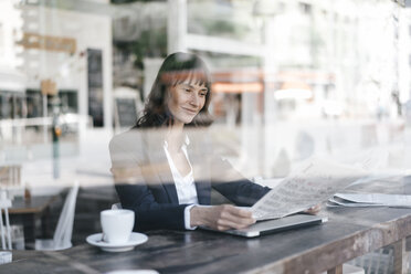 Geschäftsfrau sitzt in einem Café und liest Zeitung - KNSF01959