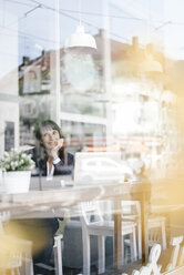 Businesswoman sitting in cafe with laptop, smiling and thinking - KNSF01968