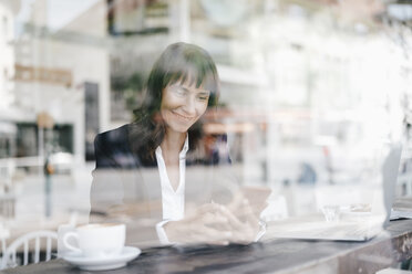 Businesswoman sitting in cafe, using smartphone - KNSF01971