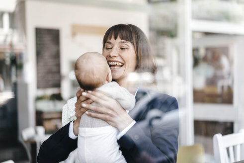 Businesswoman in cafe holding her baby - KNSF01973