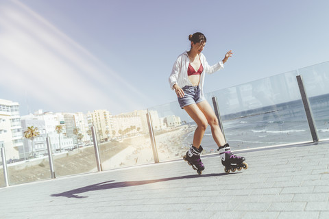 Young woman inline skating on boardwalk at the coast stock photo