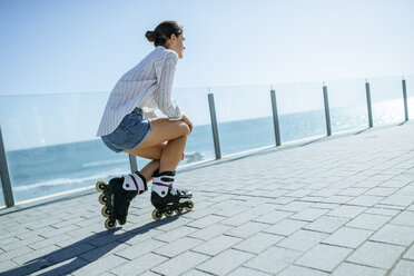 Junge Frau mit Inline-Skates auf der Strandpromenade an der Küste - KIJF01640