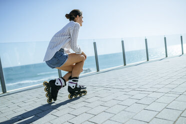 Young woman with inline skates on boardwalk at the coast - KIJF01640
