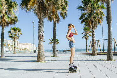 Young woman on inline skates on boardwalk with palm trees - KIJF01645