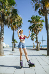 Young woman on inline skates taking a selfie on boardwalk - KIJF01646