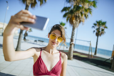 Young woman wearing yellow sunglasses taking a selfie on boardwalk - KIJF01647