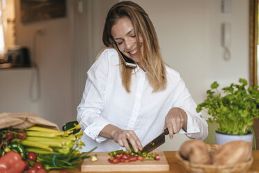 Smiling woman on the phone chopping vegetables in the kitchen - GUSF00066