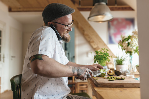 Lächelnder Mann am Telefon, der Avocado schneidet, lizenzfreies Stockfoto