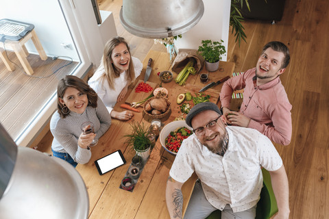 Porträt von vier Freunden, die zu Hause gemeinsam Essen zubereiten, lizenzfreies Stockfoto