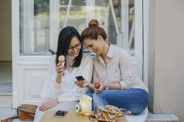 Zwei glückliche Freunde mit Eiscreme, die sich die Fotografie in der Stadt ansehen - MOMF00182