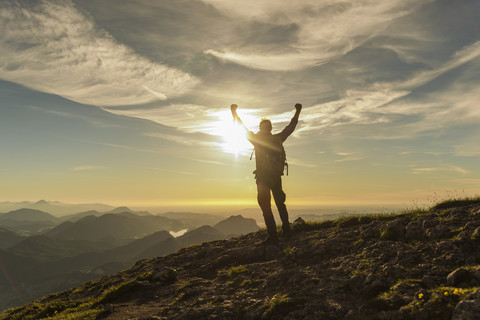 Wanderer erreicht den Gipfel und jubelt mit erhobenen Armen, lizenzfreies Stockfoto