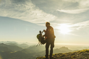 Wanderer steht auf einem Berggipfel und nimmt seinen Rucksack ab - UUF11003