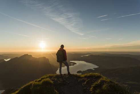 Wanderer steht auf einem Berggipfel und betrachtet die Aussicht bei Sonnenuntergang - UUF11038