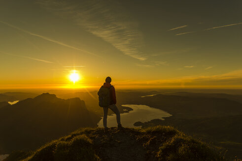Wanderer steht auf einem Berggipfel und betrachtet die Aussicht bei Sonnenuntergang - UUF11039