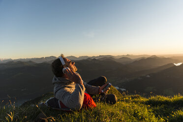 Hiker lying in grass, taking a break and listening music with headphones - UUF11044