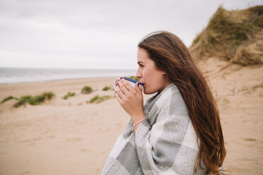 Junge Frau mit einer Tasse heißer Schokolade am Strand - NMSF00128